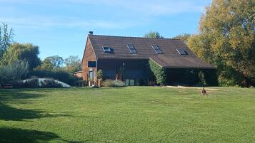 Une maison à deux étages, dotée d’un toit en pente et de lucarnes, entourée d’une pelouse bien entretenue et d’arbres.