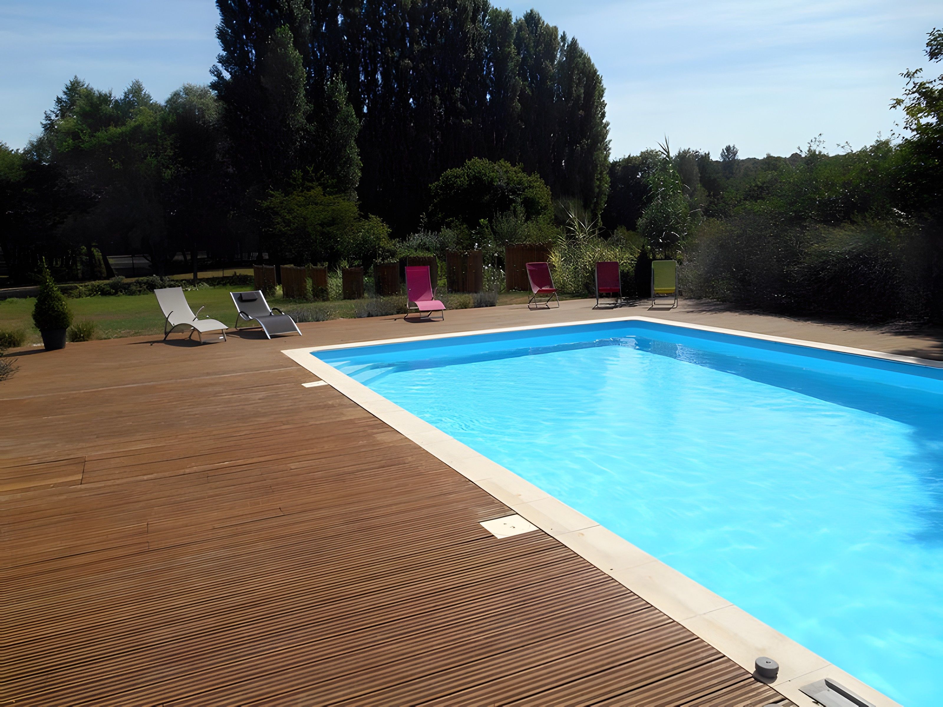 A rectangular swimming pool with a wooden deck and lounge chairs.