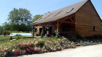 A wooden cabin with a sloped roof, a covered porch, and a garden with pink flowers.