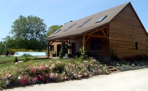 Une cabane en bois avec un toit en pente, une véranda et un jardin agrémenté de fleurs roses.