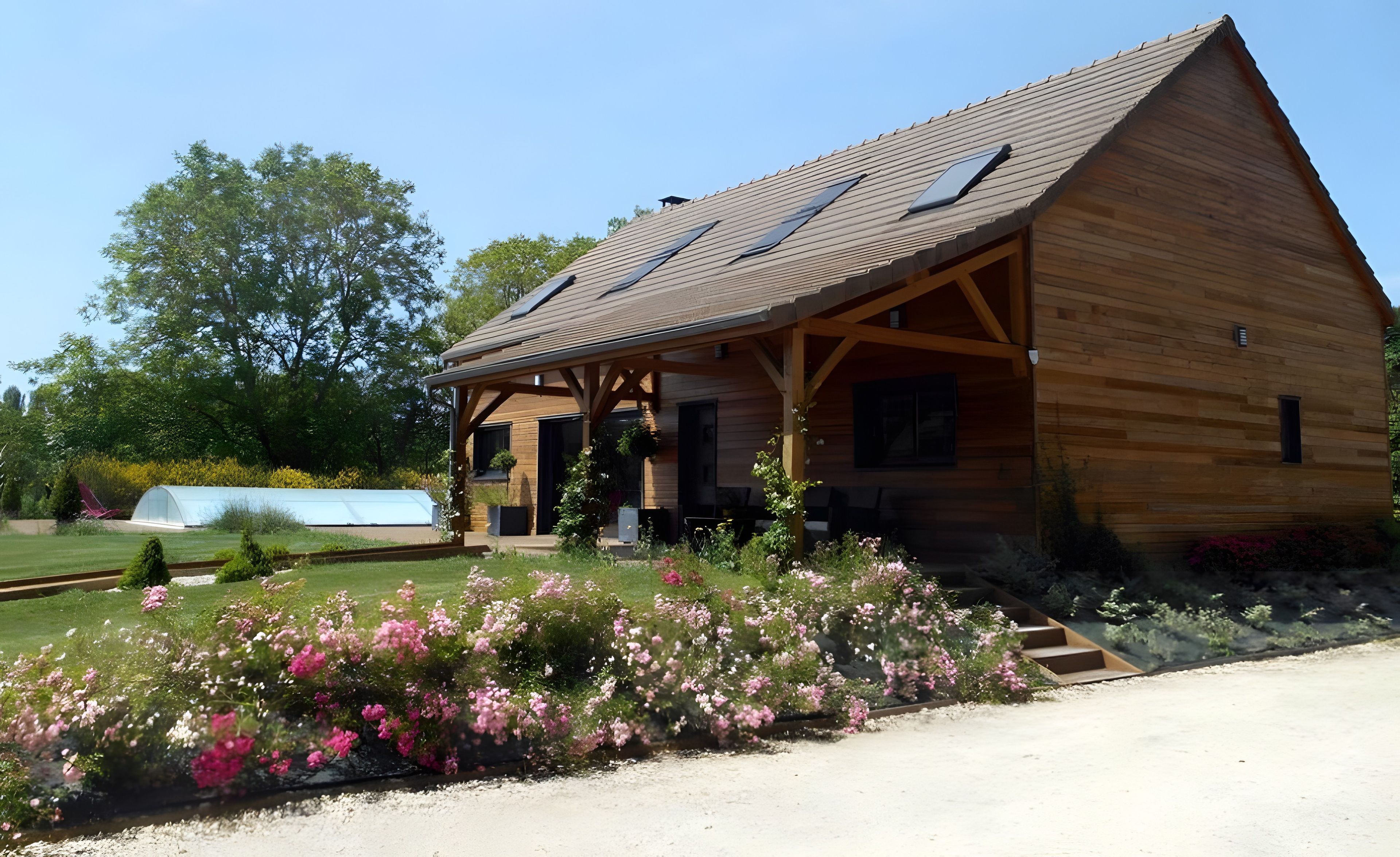 Une cabane en bois avec un toit en pente, une véranda et un jardin agrémenté de fleurs roses.