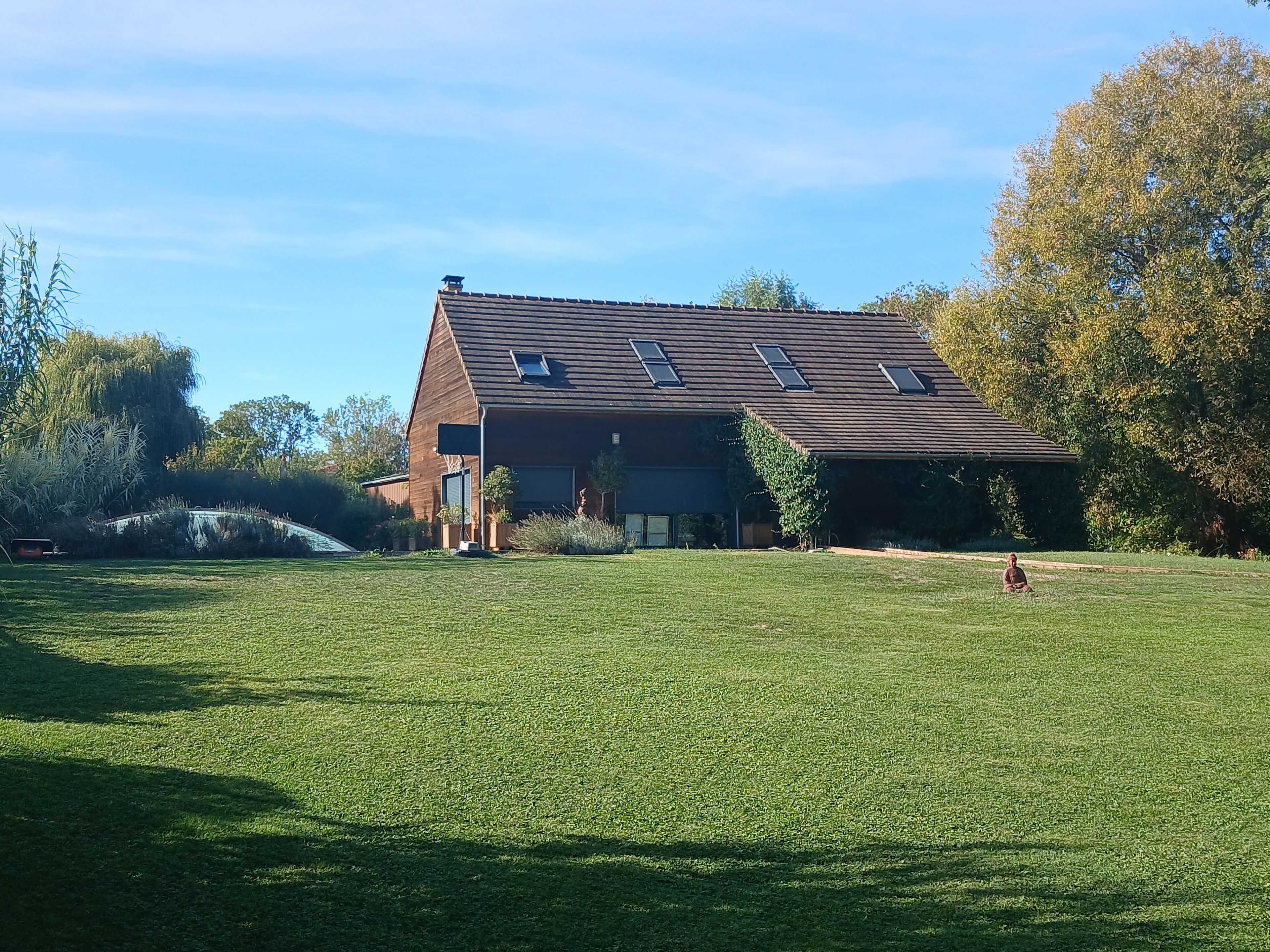 A two-story house with a sloped roof and skylights, surrounded by a well-maintained lawn and trees.