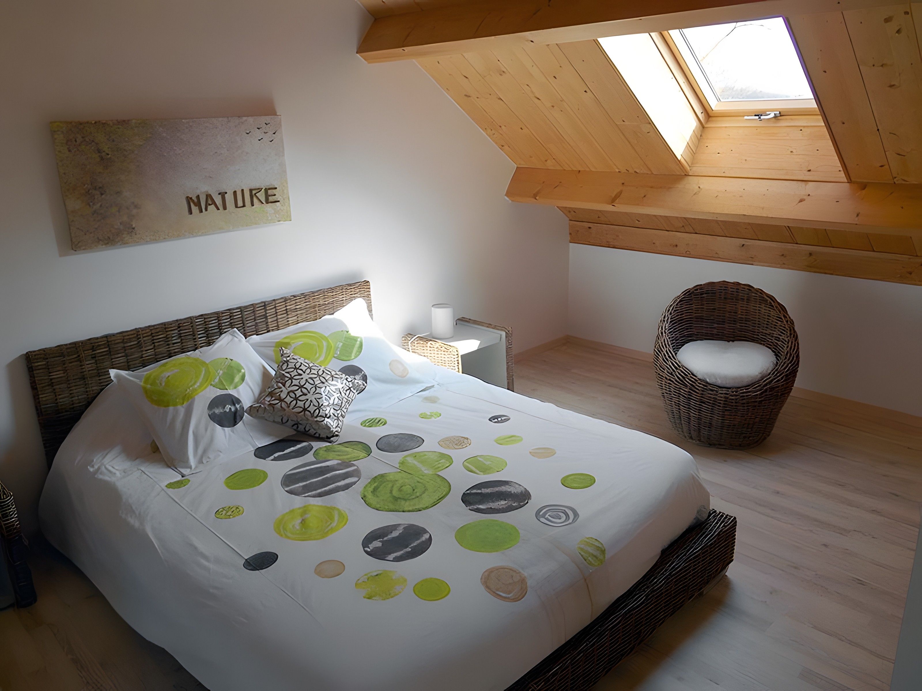 A bedroom with a bed, a wicker chair, a nightstand, and a skylight.