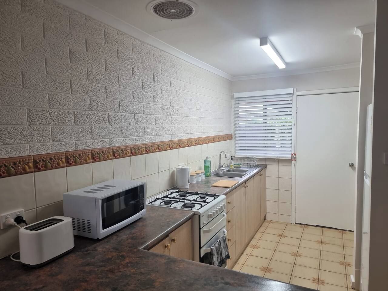 A compact kitchen with a microwave, toaster, gas stove, and a sink.