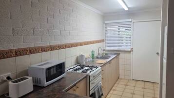 A compact kitchen with a microwave, toaster, gas stove, and a sink.