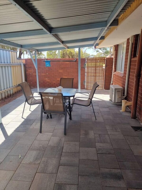A covered patio area with a table and chairs, a brick wall, and a metal gate.