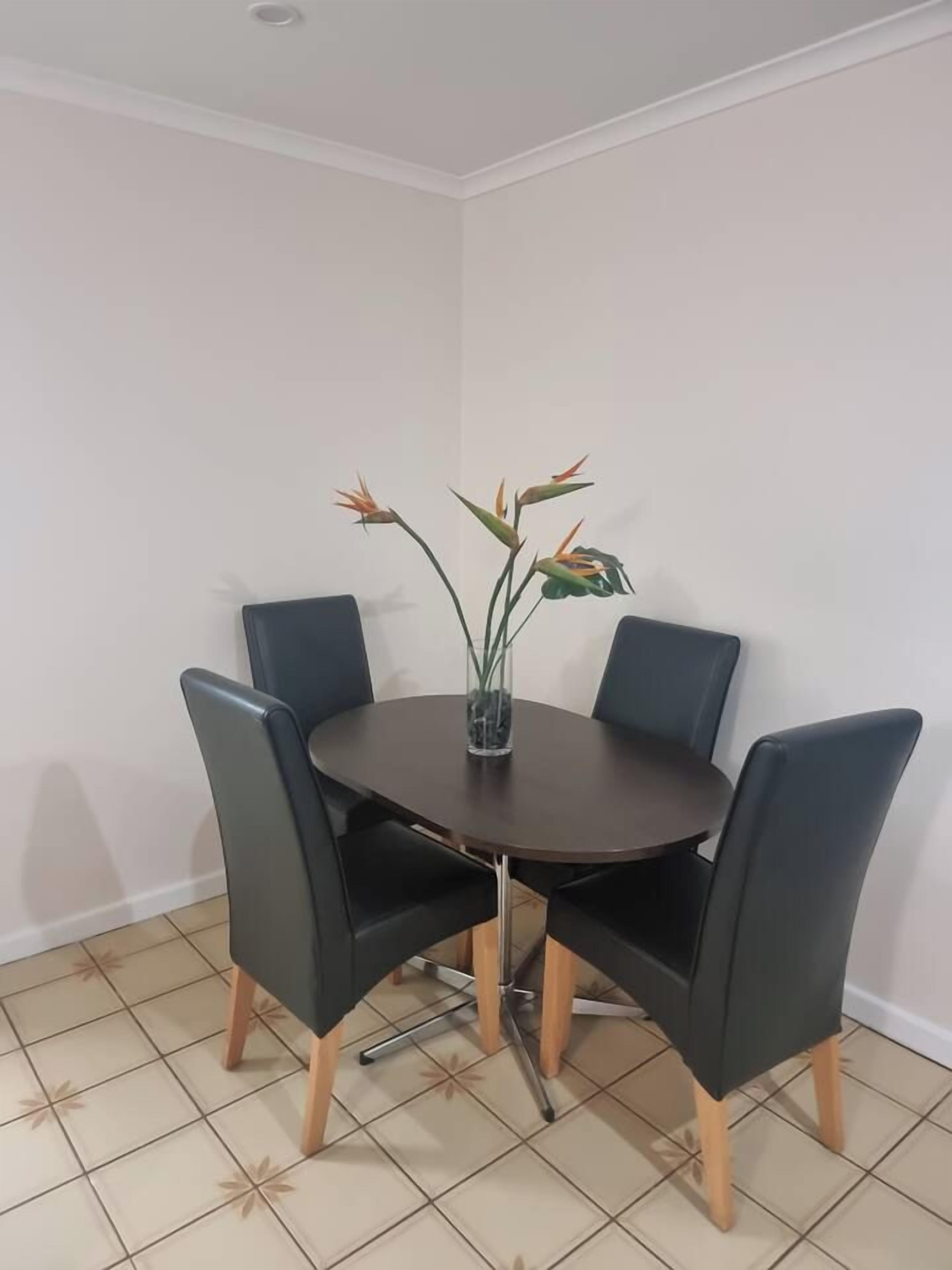 A dining area with a round table, four chairs, and a vase with flowers.