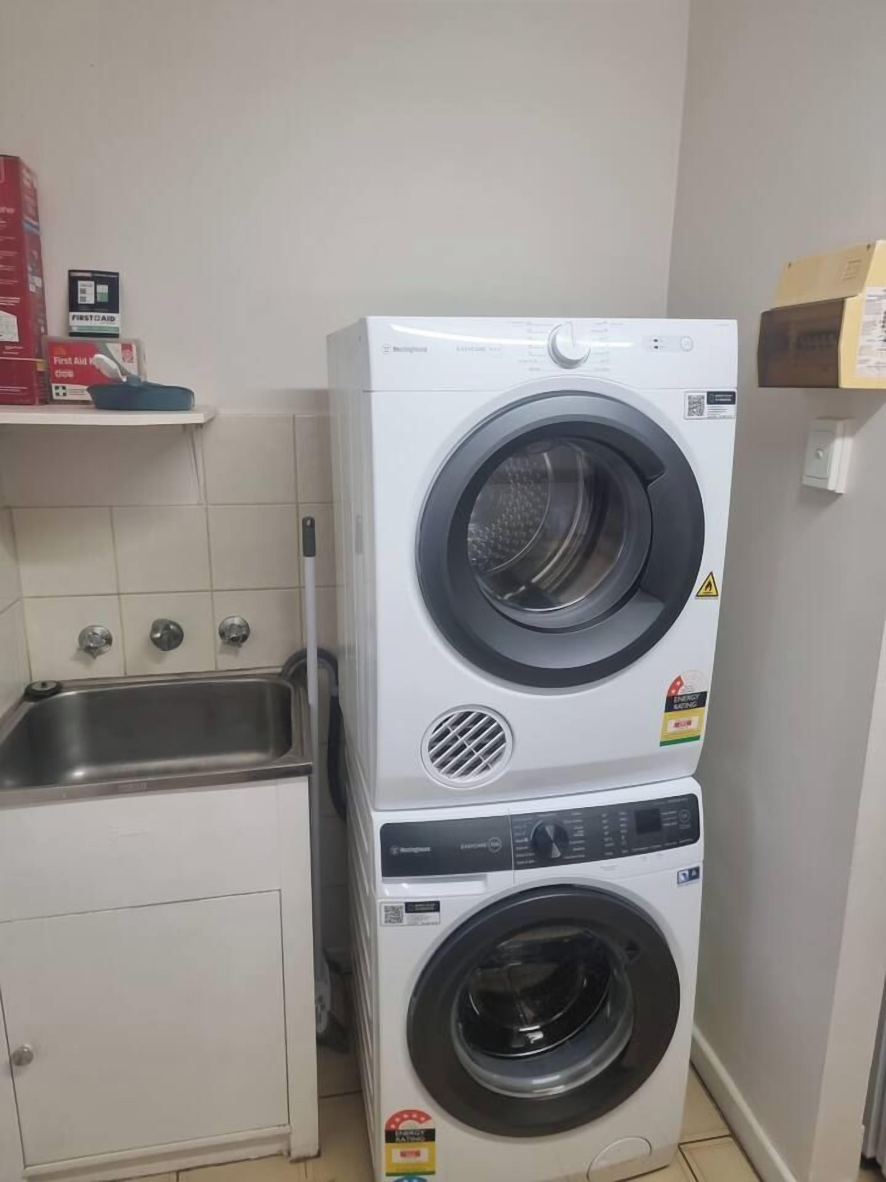 Una lavadora y secadora apiladas en un lavadero pequeño que incluye un lavamanos y un armario.