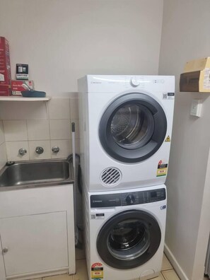 Een gestapelde wasmachine en droger in een kleine wasruimte met een wasbak en een kast.