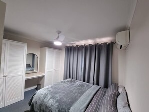 Una camera da letto con un letto, un comodino, uno specchio, una ventola a soffitto e una finestra con tende.