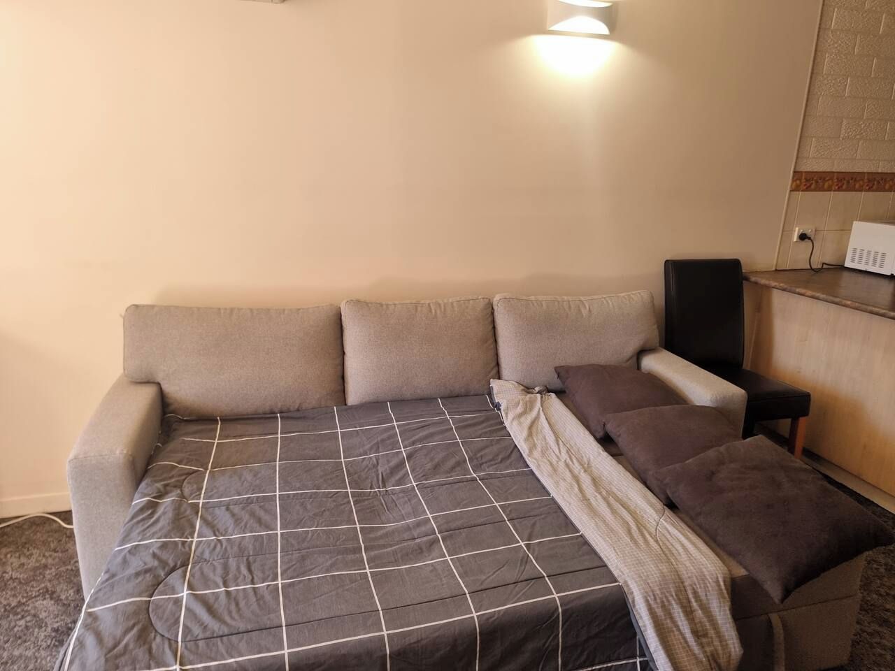 A room with a sofa bed, a blanket, and a speaker.