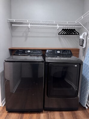 A laundry area with two front-loading washers and dryers, a metal shelf above, and a hanging rack with clothes. - Entire Home in Mount Eden, KY (Mount Eden)