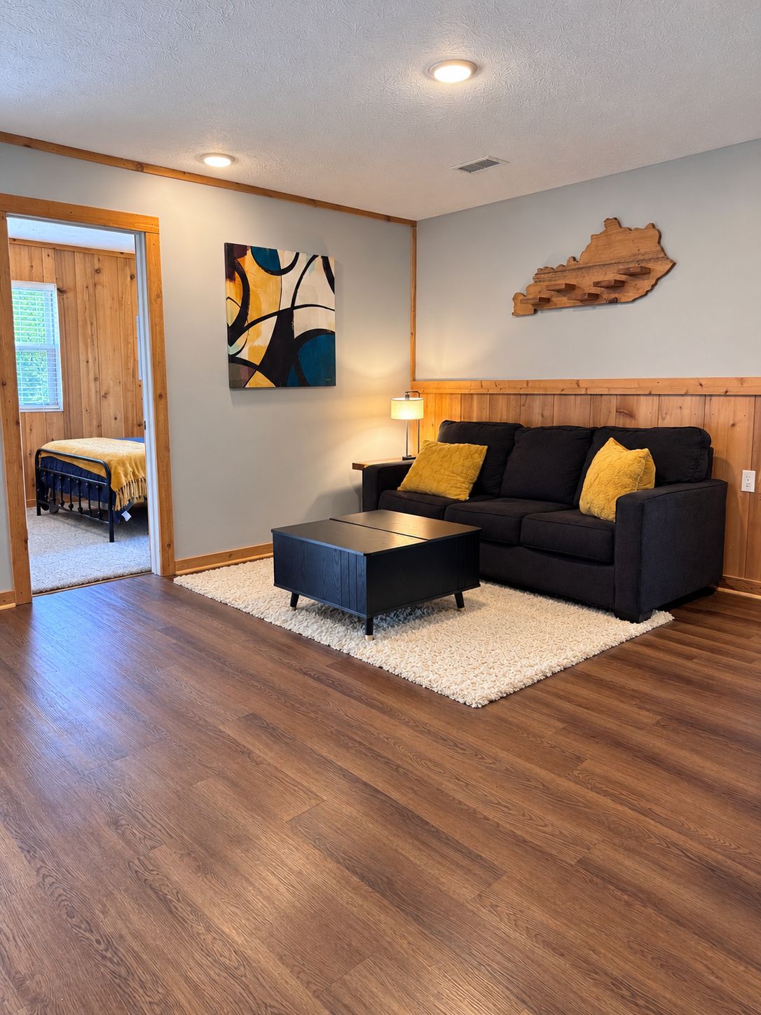 A modern living room with a dark sofa, a coffee table, and a painting on the wall.
