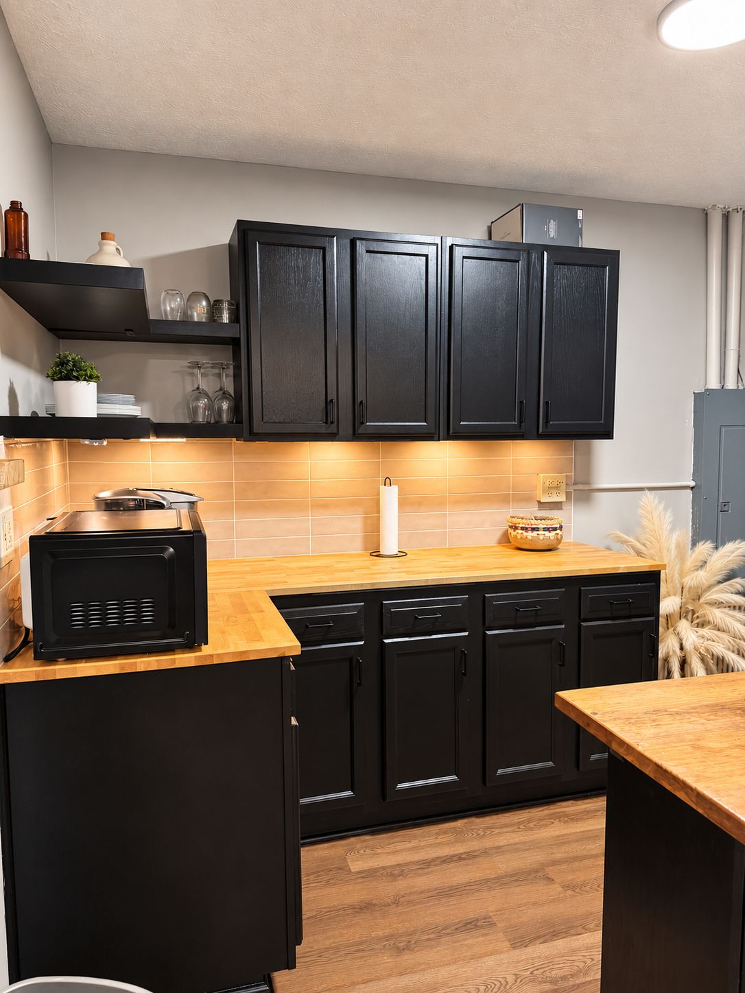 A compact kitchen with black cabinets, a microwave, and a wooden countertop.