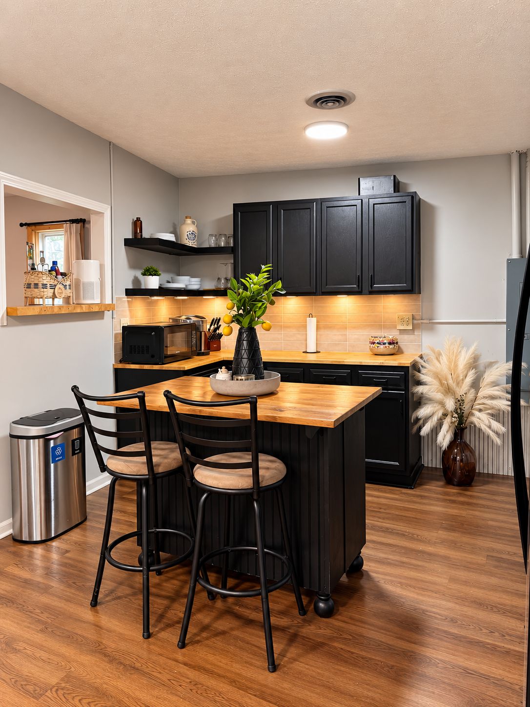 A modern kitchen with black cabinets, a wooden island, and a dining area with two chairs.