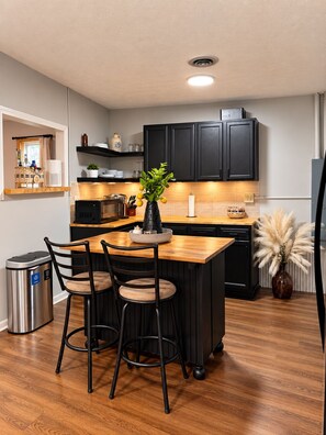 A modern kitchen with black cabinets, a wooden island, and a dining area with two chairs. - Entire Home in Mount Eden, KY (Mount Eden)