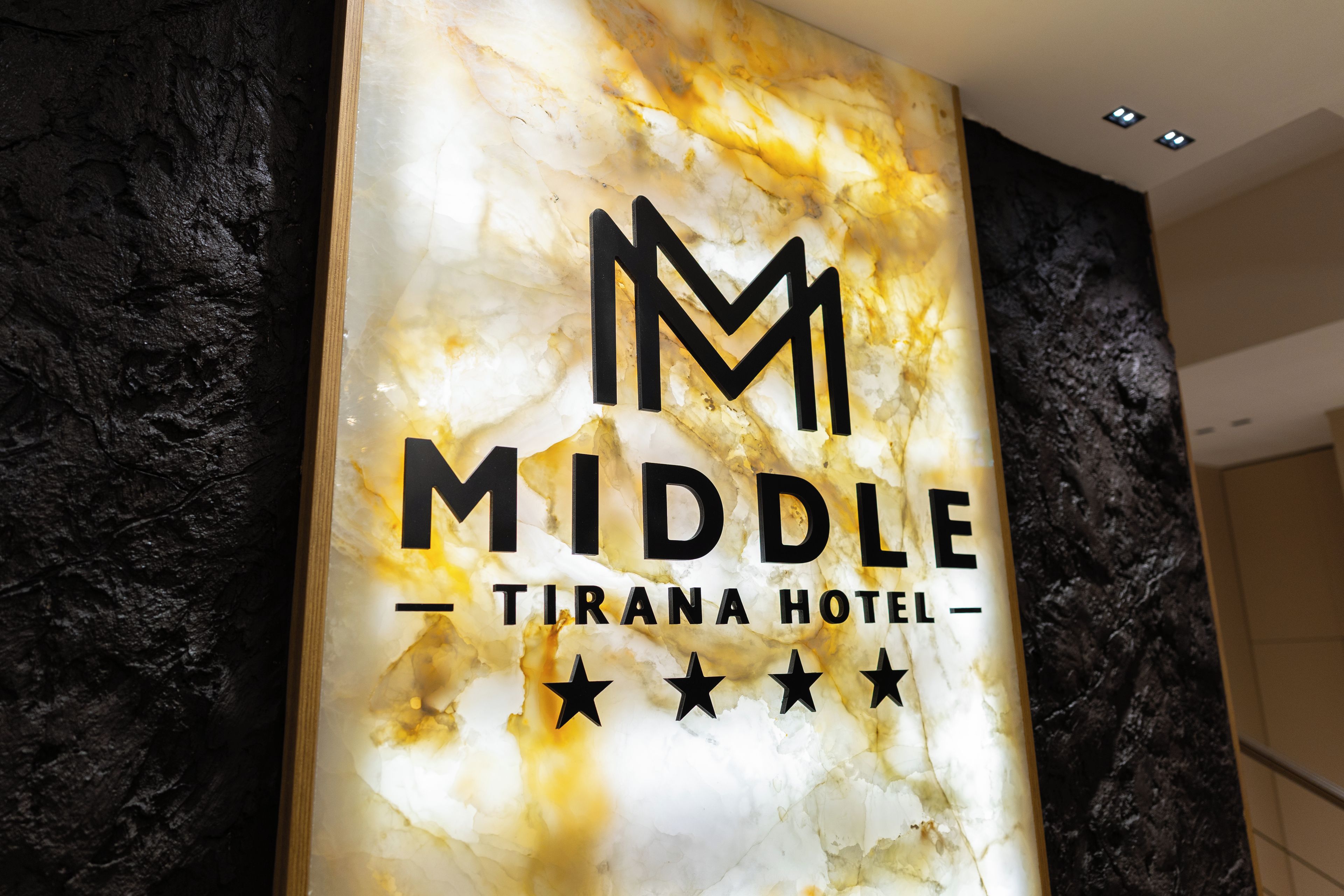 Cartel de hotel con fondo de mármol y el nombre 'MIDDLE TIRANA HOTEL', junto con tres estrellas.