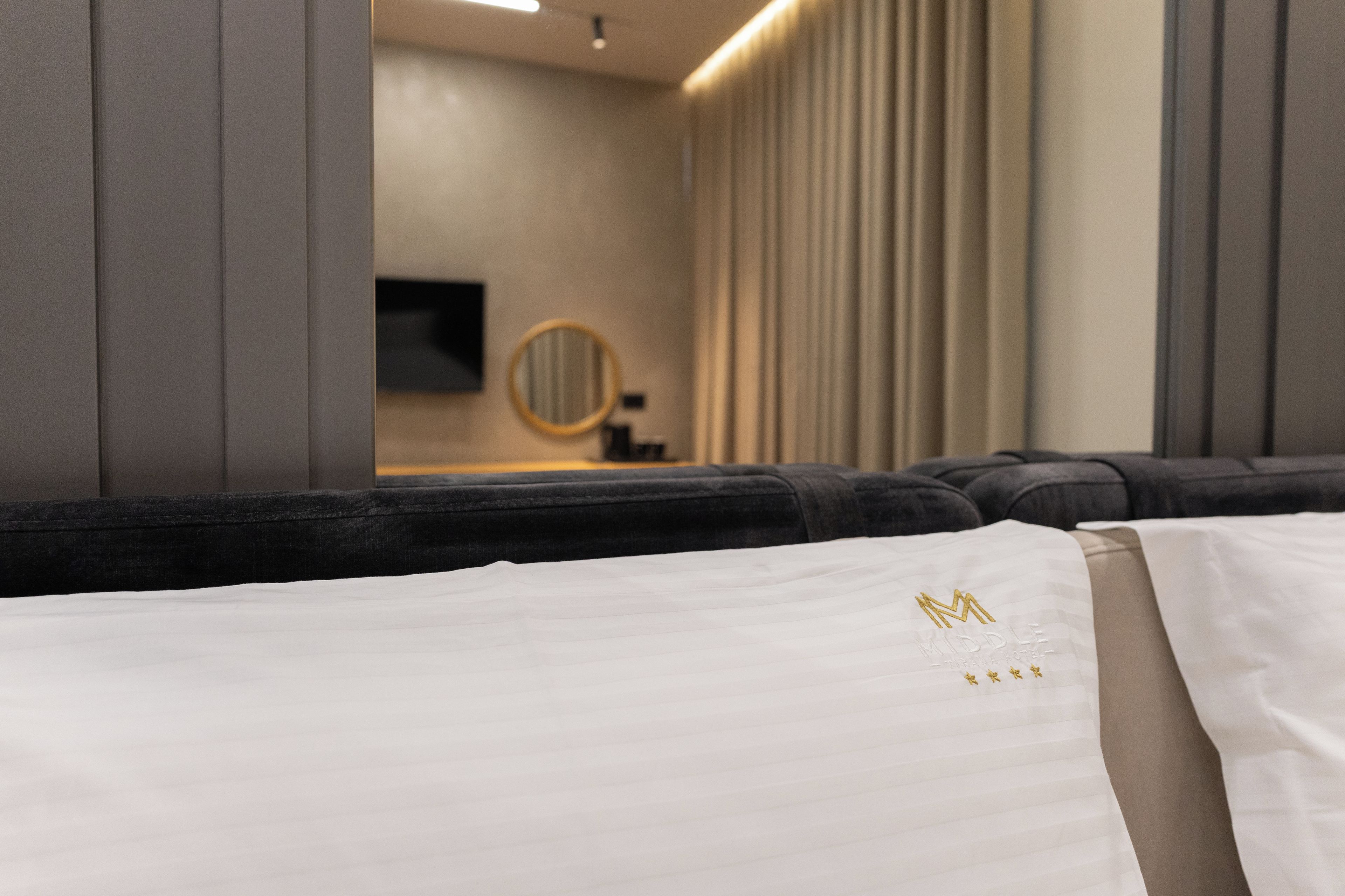 Una habitación de hotel con un sofá, una cama con almohada blanca, un espejo redondo y un televisor en la pared.