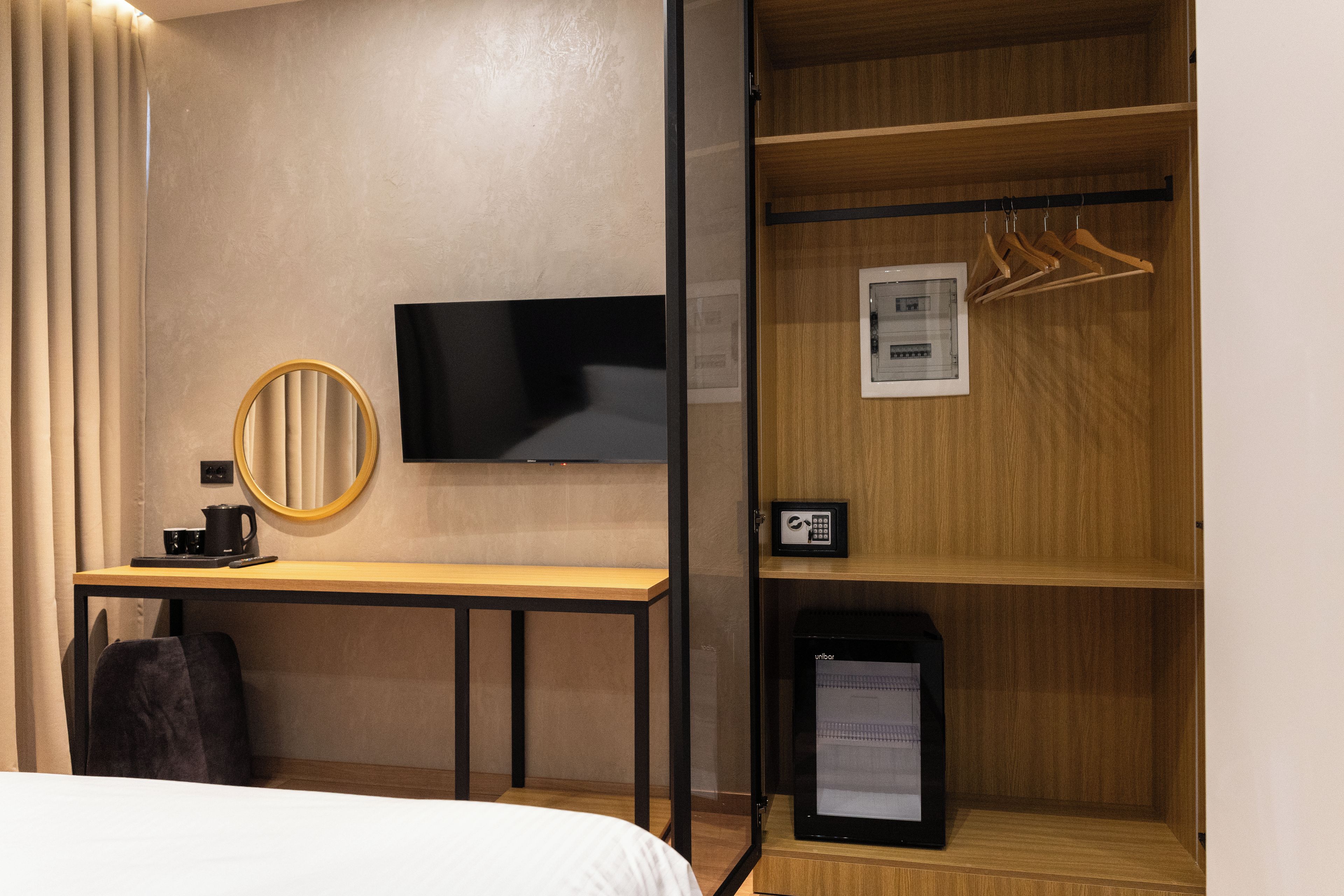 Una habitación de hotel con cama, escritorio con televisor, espejo, perchero y minibar.