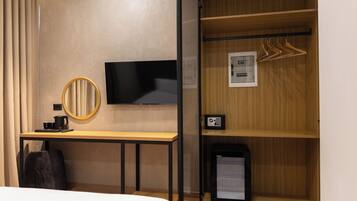 Una habitación de hotel con cama, escritorio con televisor, espejo, perchero y minibar.
