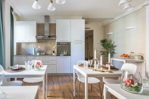 Eine moderne Küche mit weißen Schränken, einem eingebauten Backofen und einem Essbereich mit einem für vier Personen gedeckten Tisch.