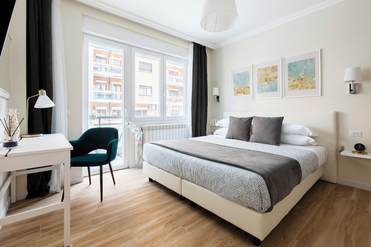 Ein modernes Hotelzimmer mit einem großen Bett, einem Schreibtisch, einem Stuhl und einem Balkon mit Blick auf die Stadt.