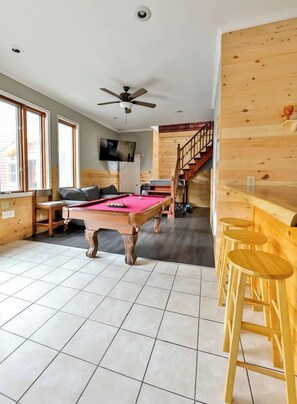 Een kamer met een pooltafel, een houten bar en een trap.