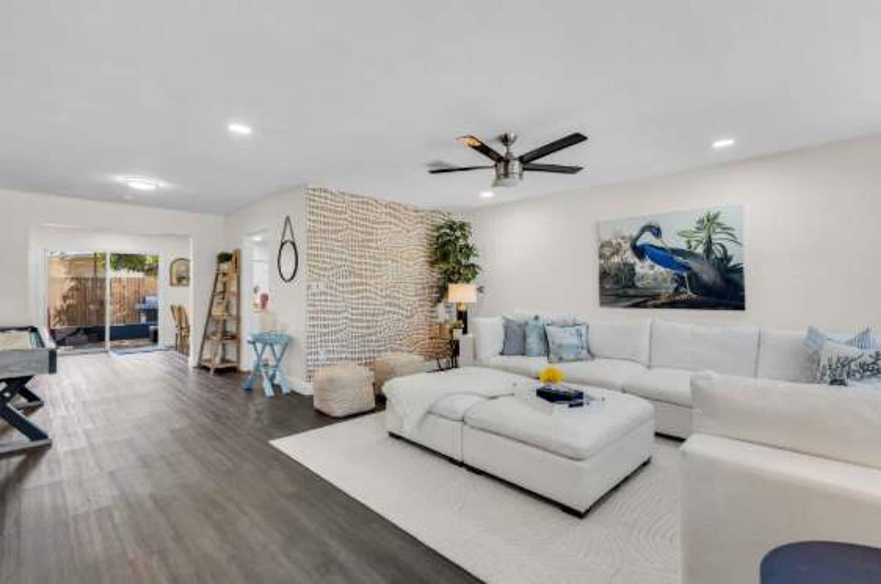 A modern living room with a white sofa, a ceiling fan, and a painting of a bird.
