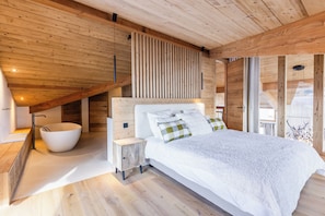 Et moderne soveværelse med en stor seng, et hvidt badekar og et skråt loft.