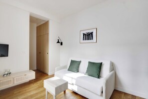 A modern living room with a white sofa, green cushions, a small white table, and a framed picture on the wall. - Modern Studio 2P - Palais Garnier (Paris)
