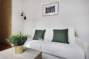 A white sofa with two green cushions, a potted plant, and a framed picture on the wall. - Modern Studio 2P - Palais Garnier (Paris)