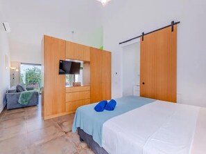 A bedroom with a bed, a TV mounted on a wooden cabinet, a sofa, and a sliding door. - Suite Robijn Luxury Accommodation (Olhao)