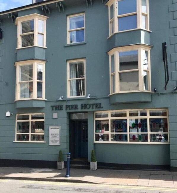 A building with a sign reading 'The Pier Hotel.' There are multiple windows with white frames, a door, and a small signboard on the wall. - The Pier Hotel (Aberystwyth)