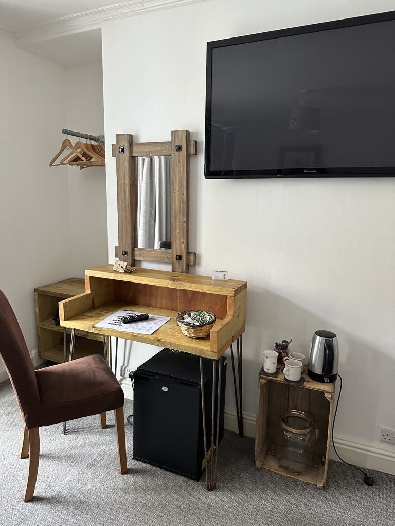 Un espacio de trabajo funcional con un escritorio de madera, una silla, un televisor montado en la pared y una mesita con una tetera y tazas.