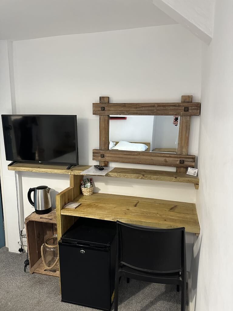 A compact room with a wooden desk, a black chair, a television, and a small refrigerator.