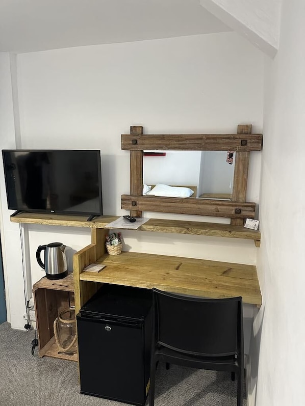 A compact room with a wooden desk, a black chair, a television, and a small refrigerator. - The Pier Hotel (Aberystwyth)