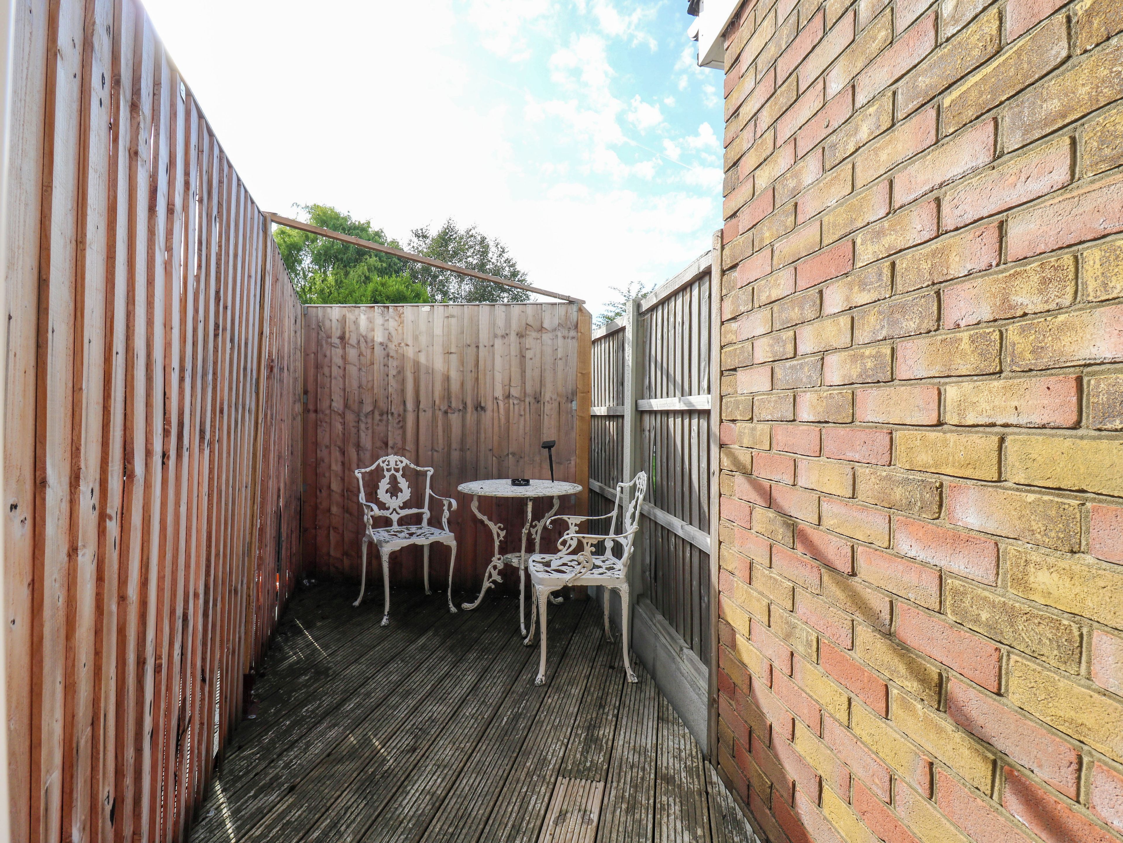 A wooden deck with two white metal chairs and a small table.