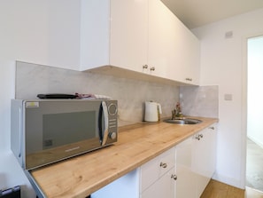 A kitchen with a microwave, wooden countertop, white cabinets, and a sink. - Annex (Southend-on-Sea)
