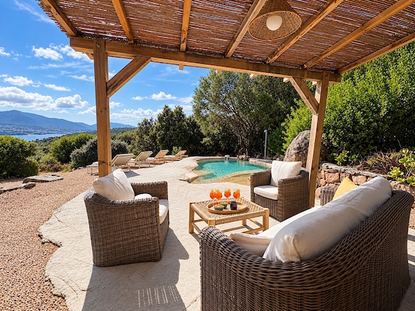 Un espacio de estar al aire libre cubierto con mobiliario de mimbre, una piscina y vistas del paisaje.