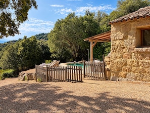 A stone building with a pool, surrounded by a wooden fence and trees. - Bergerie Babella (Olmeto)