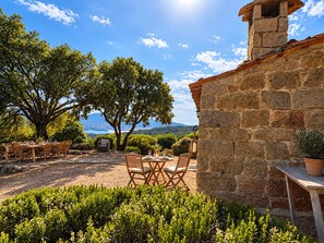 An outdoor patio with stone walls, wooden furniture, and a view of the landscape. - Bergerie Babella (Olmeto)