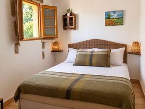 Un dormitorio con cama, ventana, armario, un cuadro y dos lámparas de pared.