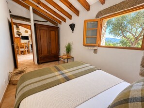 Quarto com cama, janela com vista, guarda-roupa de madeira e uma pequena mesa com uma planta.