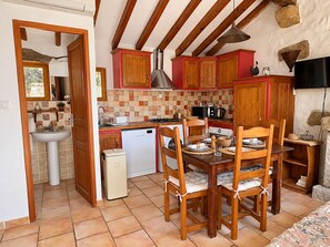 Cocina compacta con armarios de madera, una mesa de comedor con sillas, un lavamanos y un refrigerador pequeño.