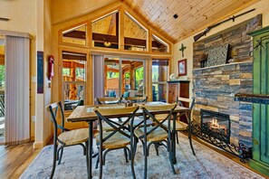 Un intérieur de chalet chaleureux avec une cheminée en pierre, une table à manger en bois et de grandes fenêtres.