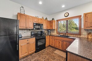 A kitchen with wooden cabinets, a black refrigerator, a microwave, an oven, and a window with blinds. - Boyne Mountain Ski/In-Out Condo W/Hot tub Sleeps 12 (Boyne Falls)