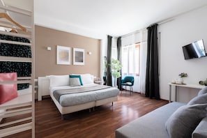 A modern hotel room with a bed, a seating area, a TV, and a wardrobe. - Momo Central Rome 3 (Roma)