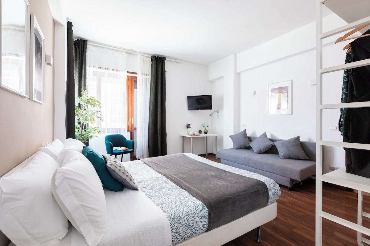 A hotel room with a bed, a sofa, a TV, a small table, and a chair.