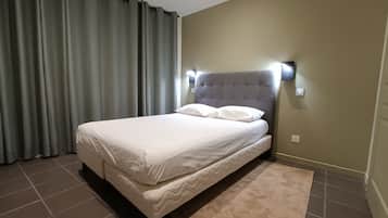 Een hotelkamer met een bed, gordijnen, een hoofdeinde met wandlampen en een vloerkleed.