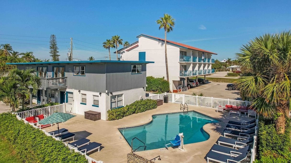 A hotel with a swimming pool, lounge chairs, and a two-story building with balconies.